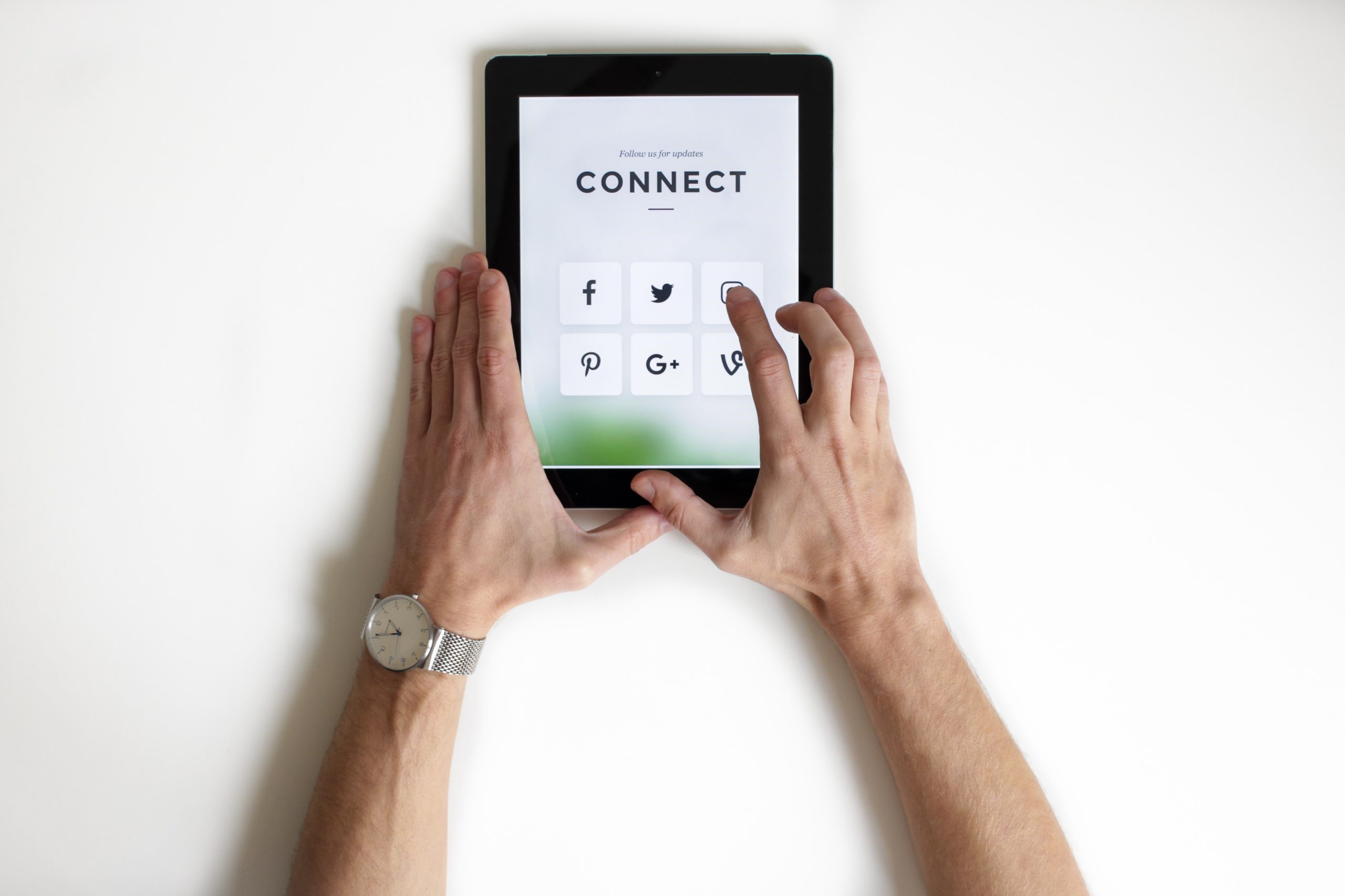 An image of a person holding an ipad in thier hands. The persons hands is tpuching the instagram icon. On the screen is "Follow us for updates: Connect" uptop. Below that is a grid of six boxes filled with 6 different social medias: facbook, twitter, instagram, pinterest, google+ and vine.